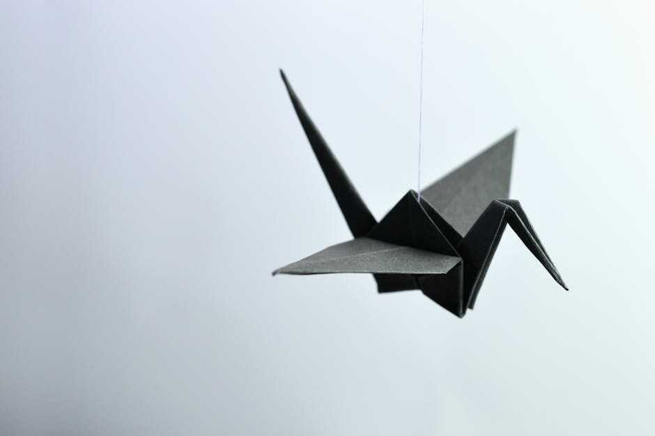 A minimalist black origami crane elegantly suspended against a soft background.